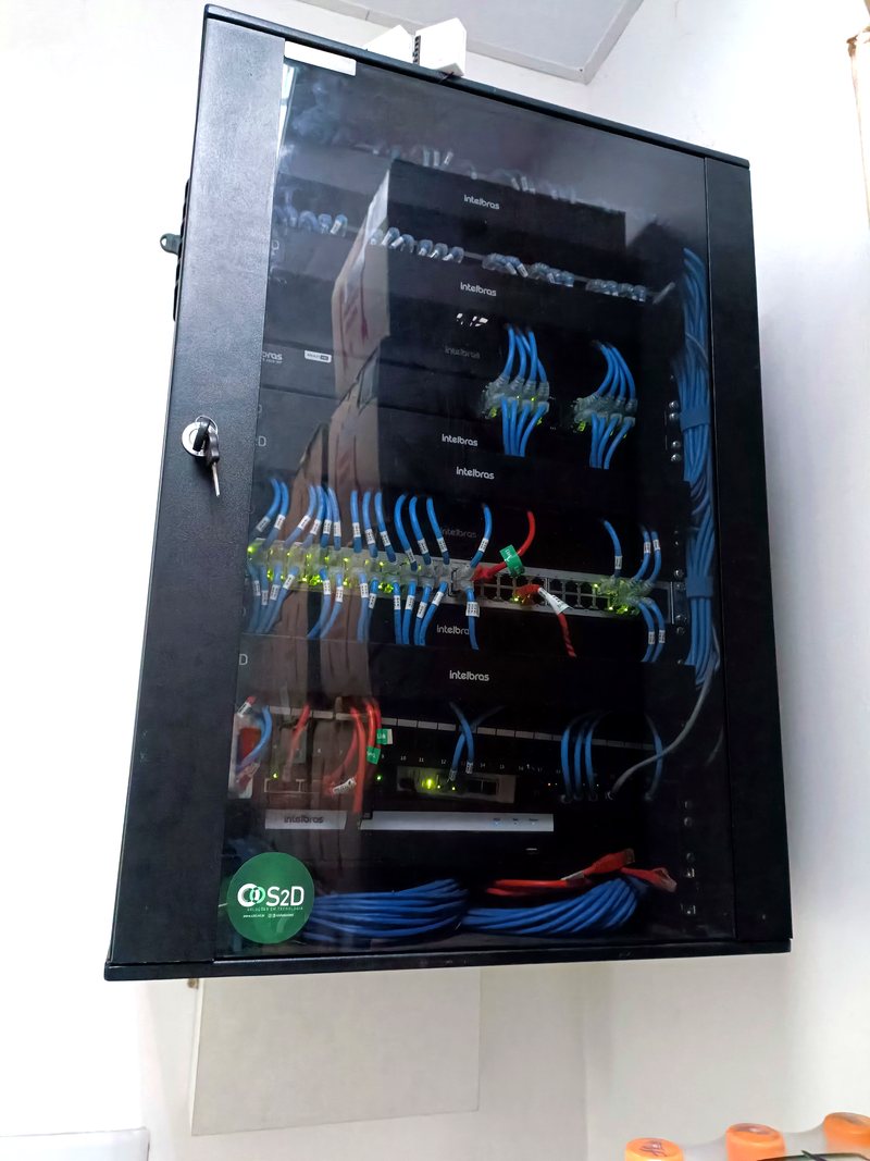 Rack de parede com cabeamento estruturado azul organizado e switches Intelbras.